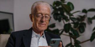 Starszy mężczyzna w okularach uśmiecha się, korzystając ze smartfona w domu