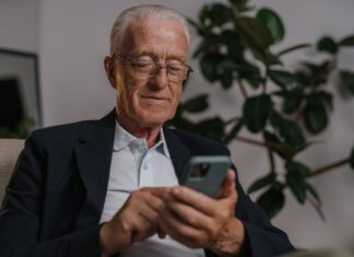 Starszy mężczyzna w okularach uśmiecha się, korzystając ze smartfona w domu