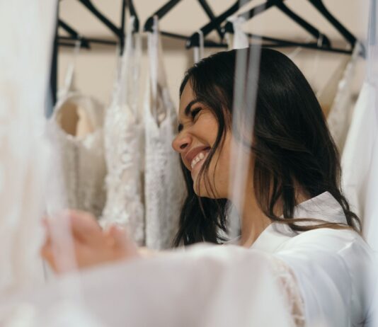 Jak wybrać idealną suknię ślubną do sylwetki i stylu wesela Uśmiechnięta panna młoda przymierza suknie ślubne w salonie bridal